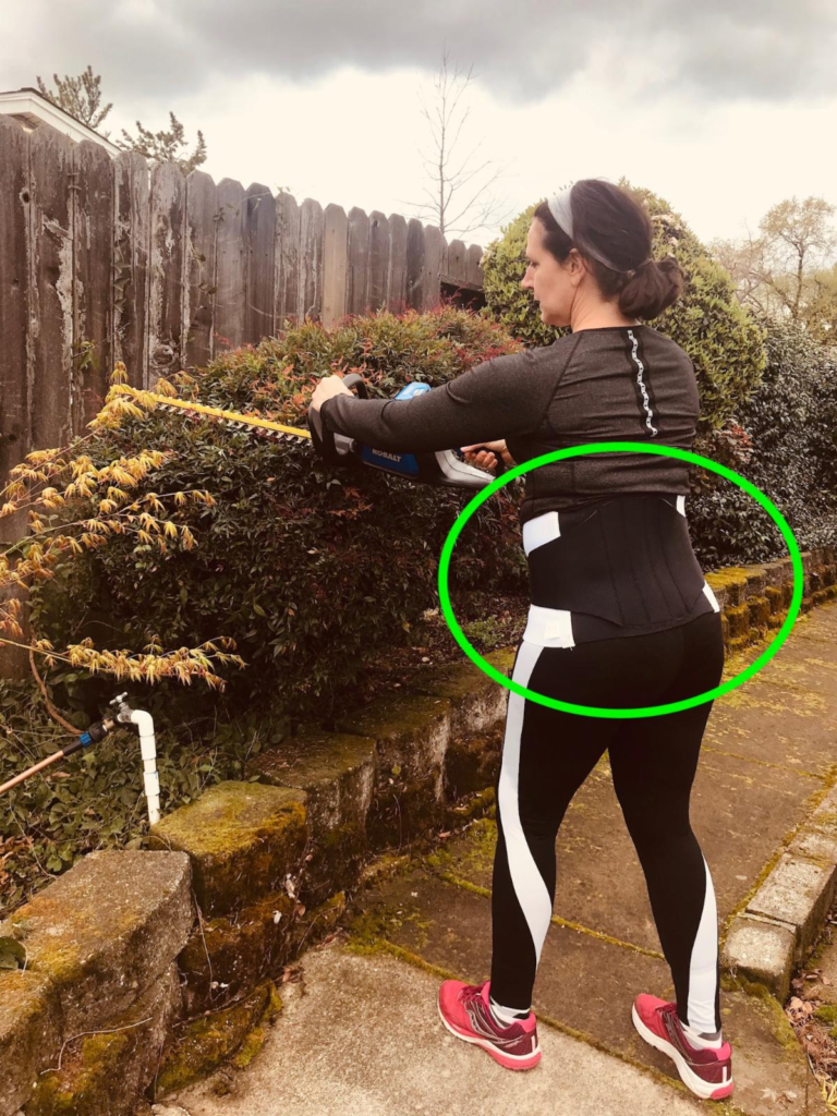 Brigit models the correct way to position your body while using a motorized hedge clipper. 