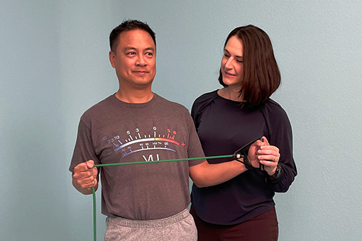 Brigit Lim instructs her patient as he stretches an exercise band with both hands. 