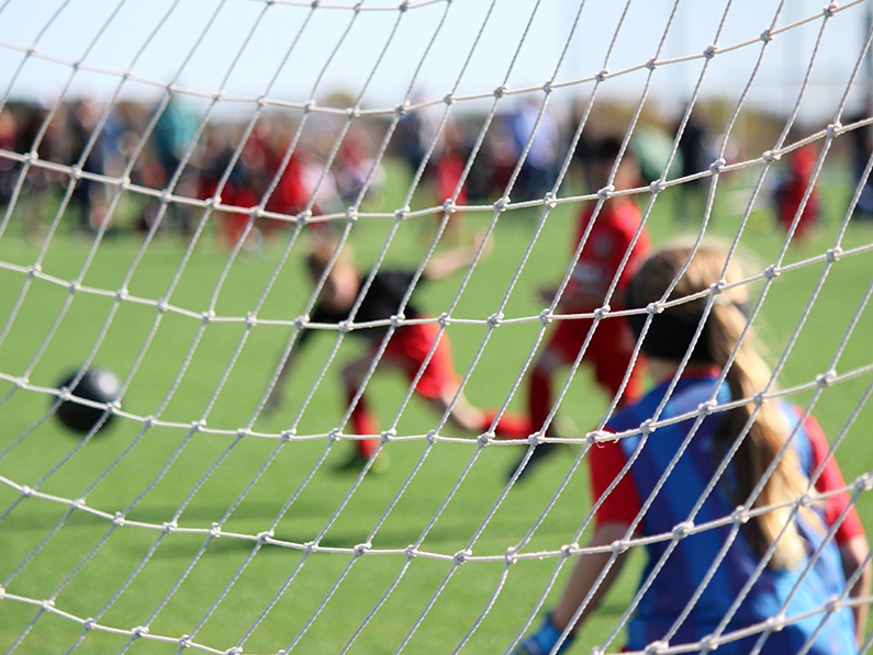 A child plays soccer goalie as another child kicks a ball in attempt to score a goal. 